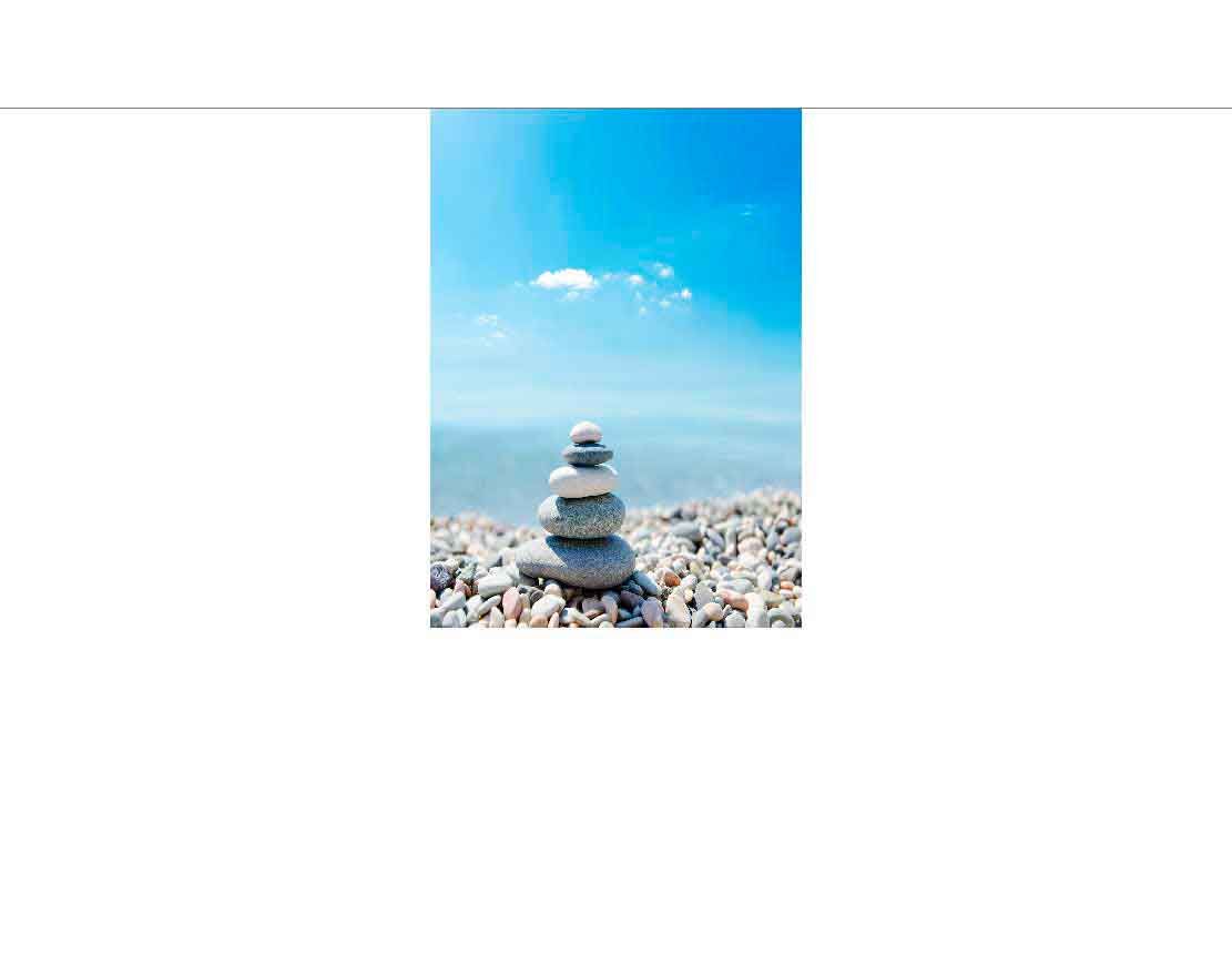 Ein Stapel aus flachen, runden Steinen auf einem Kiesstrand mit blauem Himmel im Hintergrund
