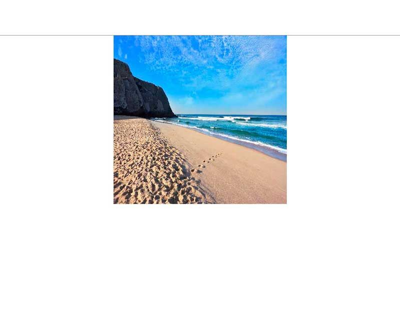 Eine ruhige Küstenszene mit Sandstrand, Felsenküste und einem klaren blauen Himmel.