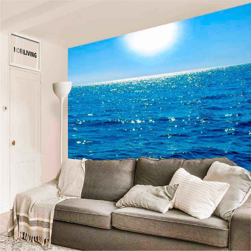 Ein Wohnzimmer mit einem grauen Sofa und einer beeindruckenden Fototapete eines blauen Ozeans unter sonnigem Himmel.