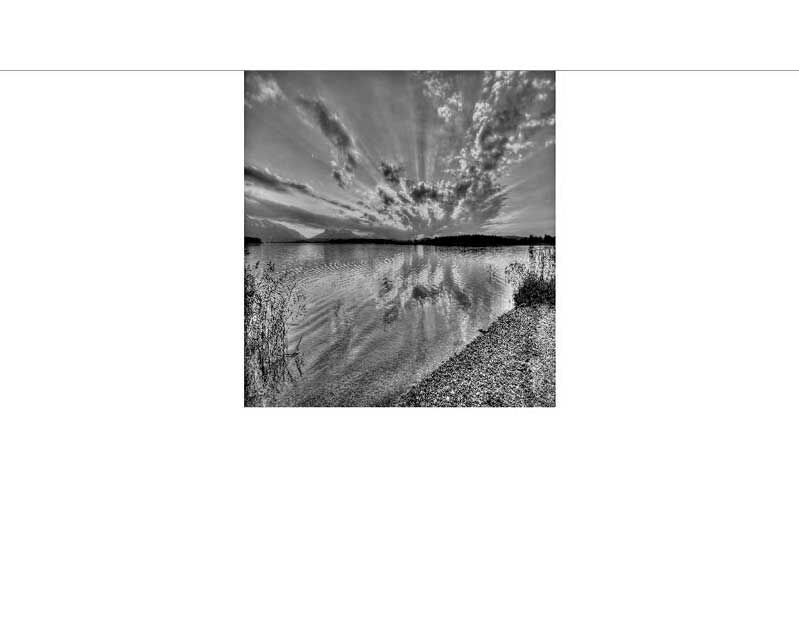 Schwarzweißfoto eines Sees mit Wolkenspiegelung und Kieselstrand