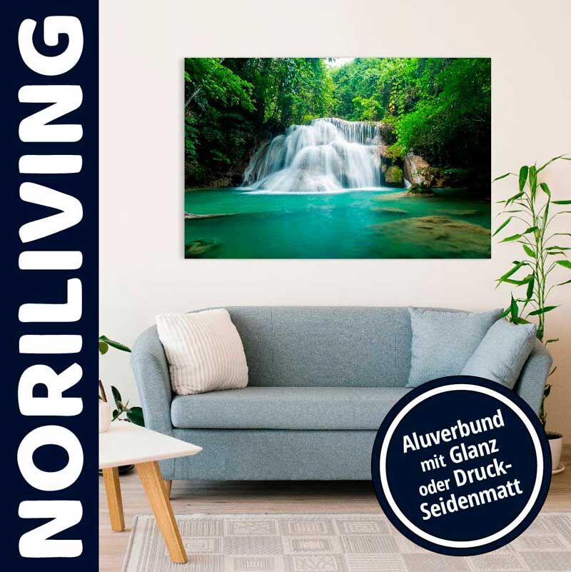 Ein Wandbild mit einem Wasserfallmotiv hängt über einem hellgrauen Sofa in einem stilvollen Wohnzimmer, auf dem ein Kissen liegt. Linkerhand sieht man den Schriftzug 'Noriliving'. Im Vordergrund eine Zimmerpflanze.