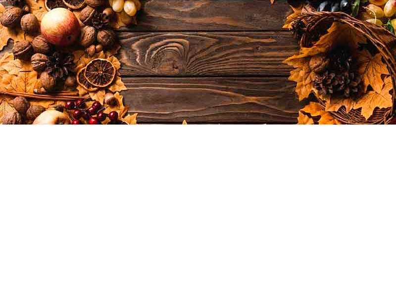 Ein herbstliches Arrangement aus Nüssen, getrockneten Orangen, Tannenzapfen und Laub auf einem Holztisch.