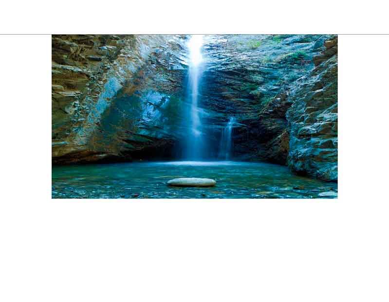Ein klarer Wasserfall fließt in einem von Felsen umgebenen Pool in einer ruhigen, natürlichen Umgebung.