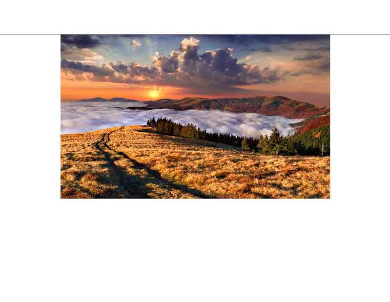 Ein malerischer Sonnenuntergang über einem Landschaftspanorama mit Nebel, Bergen und einem Wiesenpfad.