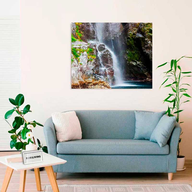 Helles Wohnzimmer mit hellblauem Sofa, darauf zwei Kissen, und einem großen Wasserfallbild an der Wand. Daneben stehen Pflanzen und ein Couchtisch.