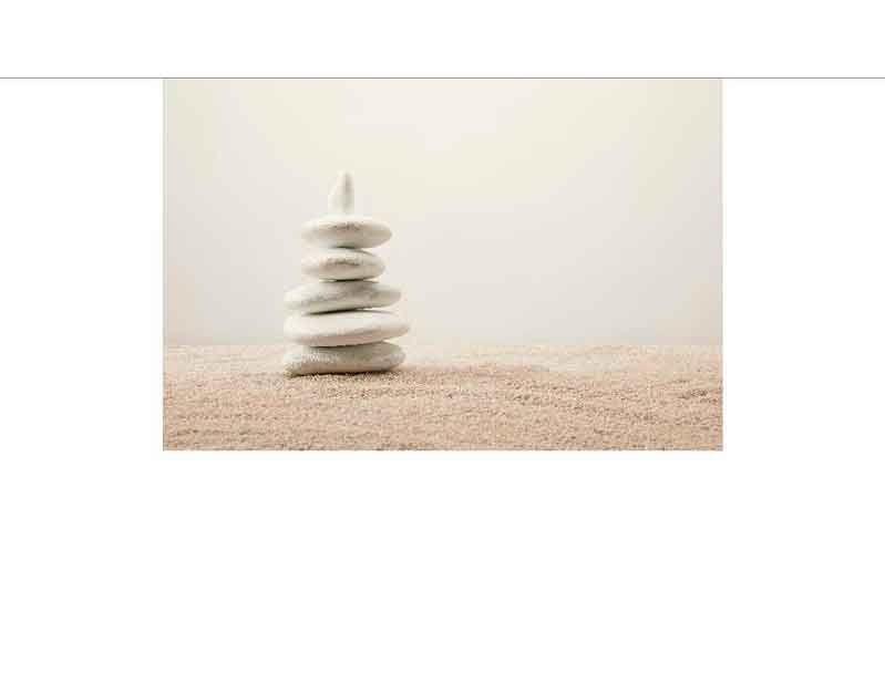 Eine kleine Pyramide aus weißen Steinen auf sandigem Untergrund, die Balance und Ruhe symbolisiert.