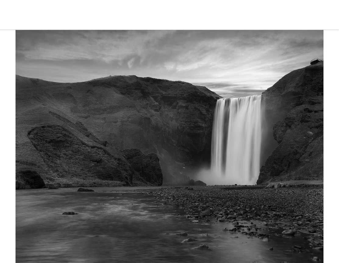 Ein majestätischer Wasserfall fließt über eine steile Felswand in einer malerischen Landschaft in einem Schwarz-Weiß-Foto.