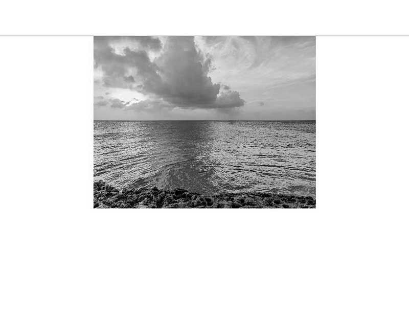 Schwarz-Weiß-Bild des Ozeans mit dramatischen Wolken über dem Horizont, aufgenommen von einer felsigen Küste aus
