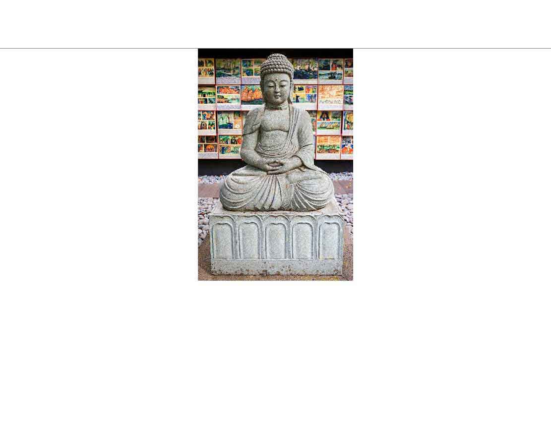 Große Steinbuddha-Statue vor einer bunten Wand voller Kunstwerke