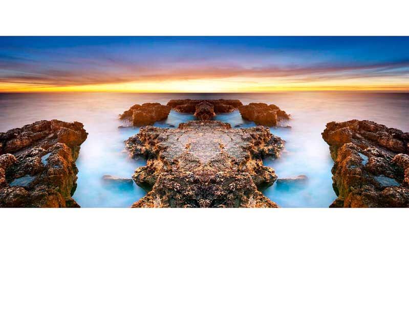 Ein atemberaubender Sonnenuntergang über einer felsigen Küstenlinie, die ins Meer führt, mit einem farbenfrohen Himmel im Hintergrund.