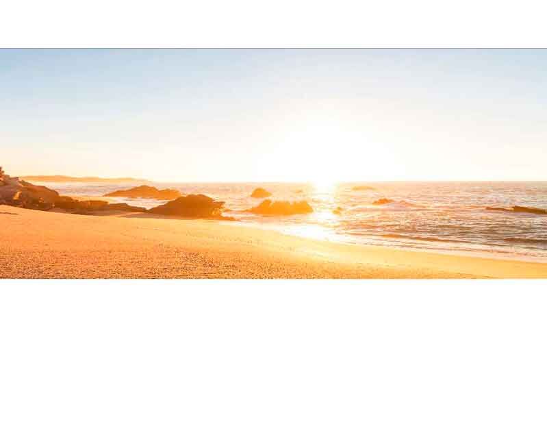 Ein goldener Sonnenuntergang über einem einsamen Strand mit sanften Wellen und Felsen im Hintergrund