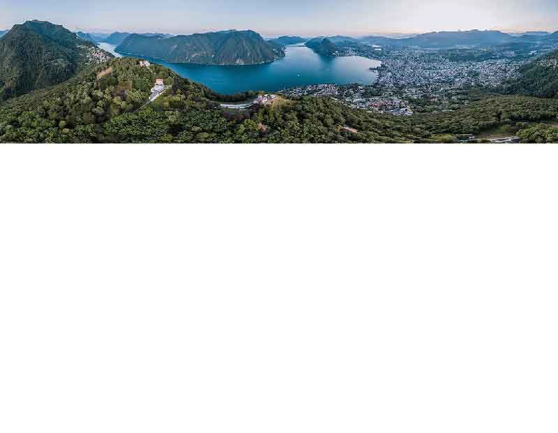 Panoramaaufnahme des Lugano-Sees mit der Stadt und den umliegenden Bergen im Hintergrund