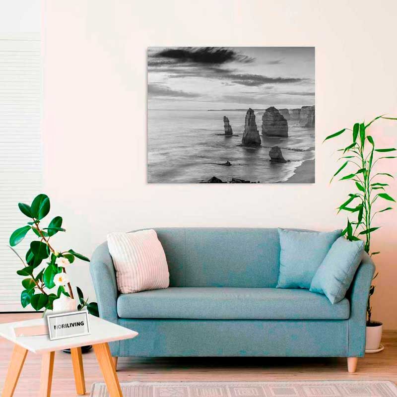 Ein gemütliches Wohnzimmer mit einem blauen Sofa und einem Schwarz-Weiß-Bild an der Wand, das Felsformationen im Meer zeigt.
