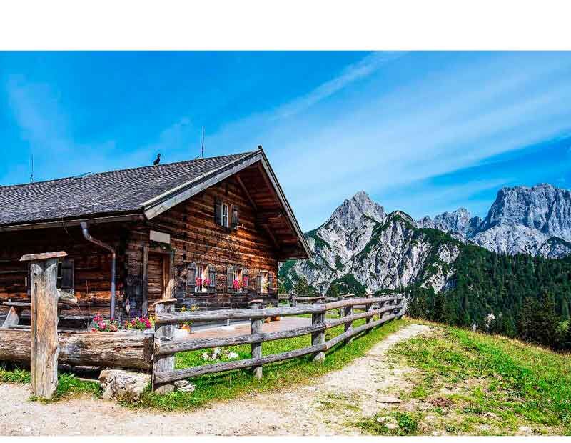 Holzhütte in den Alpen mit Blick auf eindrucksvolle Bergketten und blauen Himmel