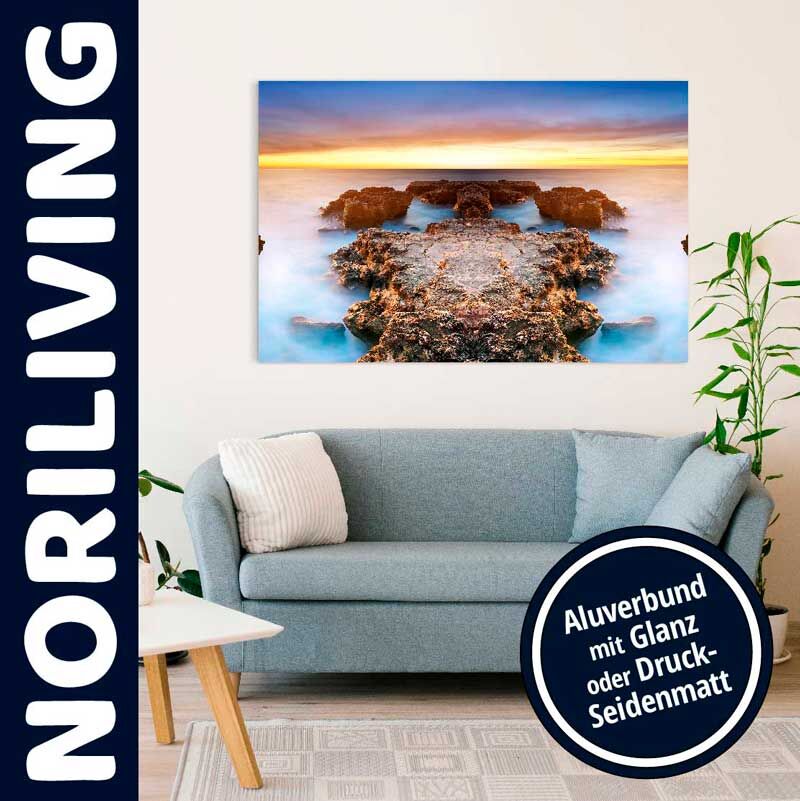 Wohnzimmer mit stilvollem Sofa und farbenfrohem Alu-Dibond-Bild, das eine natürliche Küstenszene bei Sonnenuntergang zeigt