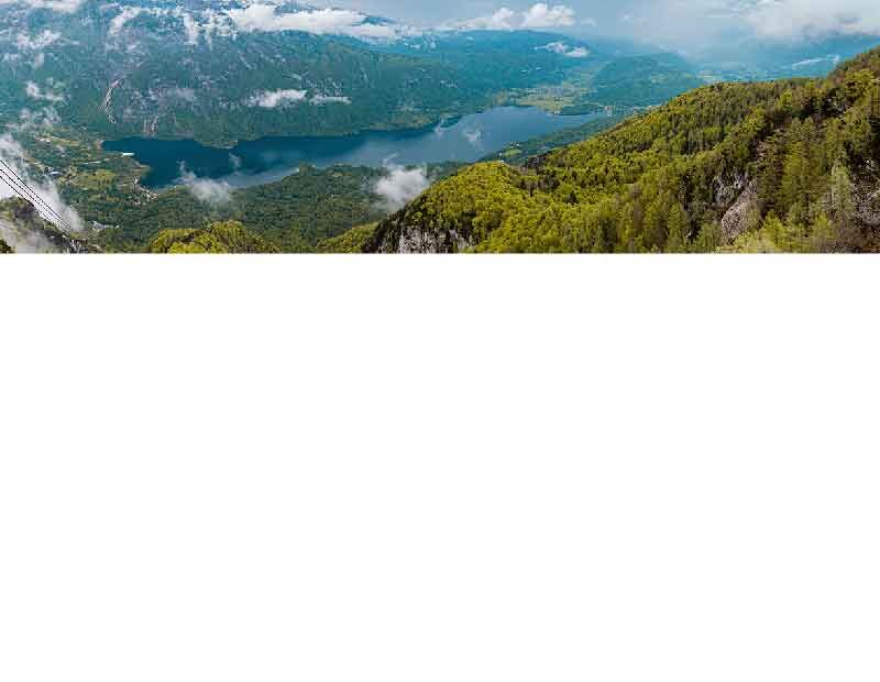 Luftaufnahme einer grünen Berglandschaft mit einem großen See und Wolken am Himmel