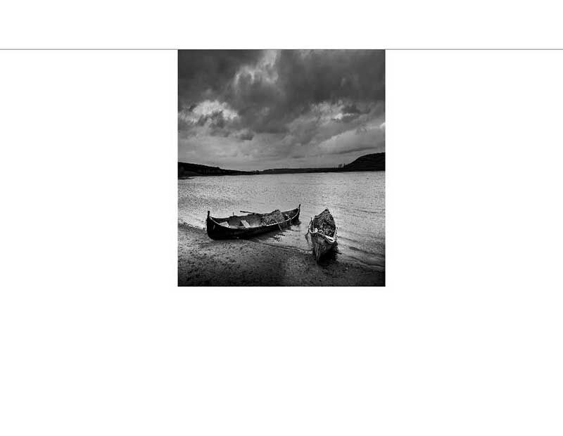 Schwarzweißfoto von zwei Booten am Ufer eines Sees mit dramatischem Himmel