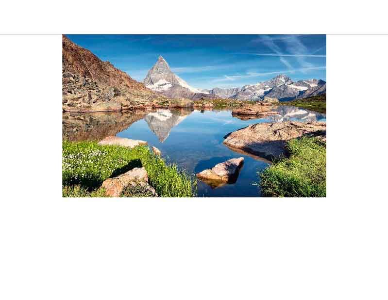 Kristallklarer Bergsee mit dem Matterhorn und umliegenden Bergen, reflektiert im Wasser, umgeben von grünen Wiesen und Felsen, unter blauem Himmel