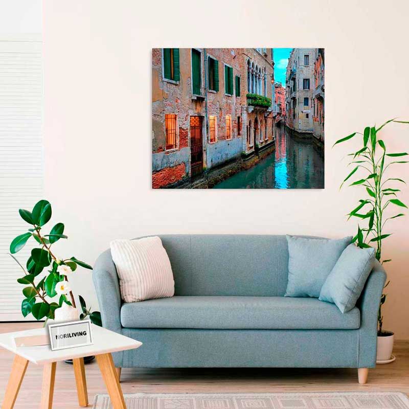 Ein gemütliches Wohnzimmer mit einem blauen Sofa, dekoriert mit einem großen Leinwandbild, das eine malerische Szene aus Venedig zeigt. Die warmen Farben des Bildes ergänzen perfekt das moderne Ambiente des Raums.