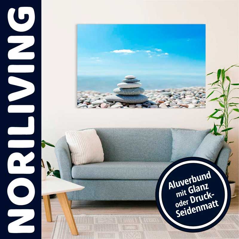 Stilvolles Wohnzimmer mit blauer Couch, Pflanze und Leinwandbild eines Steinstapels am Strand vor blauem Himmel