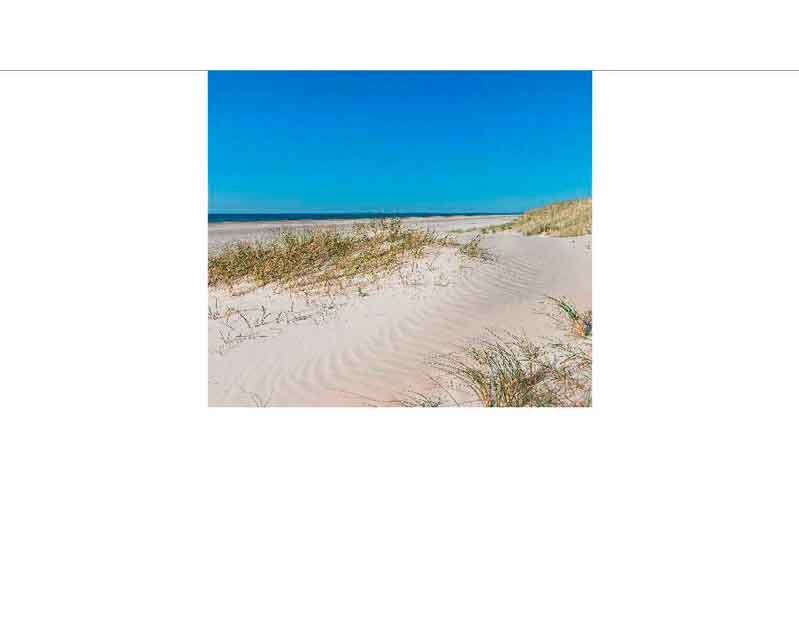 Ein ruhiger Strand mit feinem Sand, Dünen und blauem Himmel
