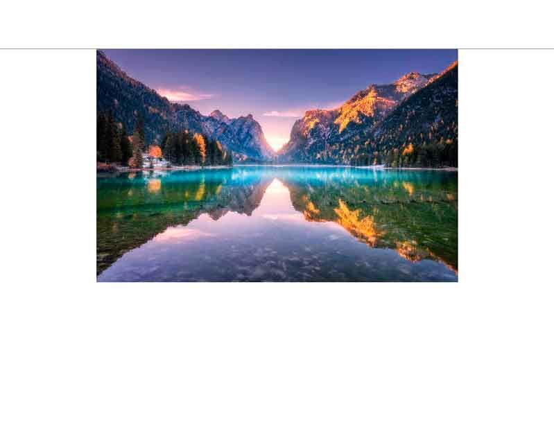 Ein klarer Bergsee spiegelt die umgebenden Berge und den bunten Sonnenuntergang wider, umgeben von einer idyllischen Waldlandschaft.