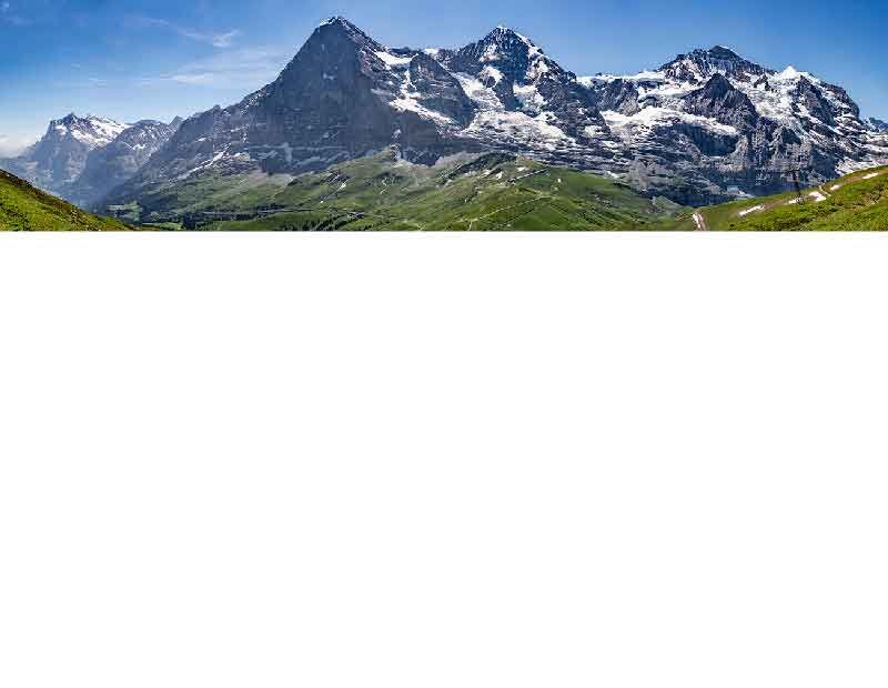 Beeindruckende Ansicht von verschneiten Bergen und grünen Tälern unter blauem Himmel