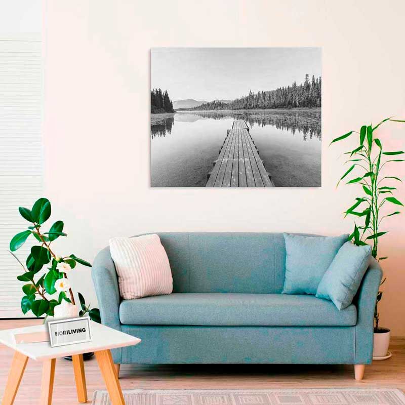Wohnzimmerdekor mit einem blauen Sofa, dekorativen Kissen und einem schwarz-weißen Wandbild eines Holzstegs an einem ruhigen Seeweg