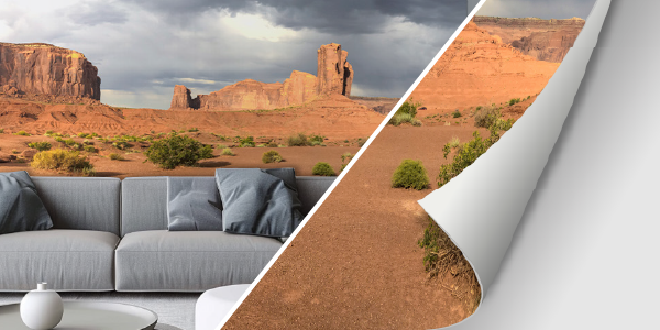 Ein Wohnzimmer mit einer großen Landschaftstapete, die eine beeindruckende Wüstenlandschaft zeigt. Die gemütliche Einrichtung umfasst ein graues Sofa und Dekokissen.