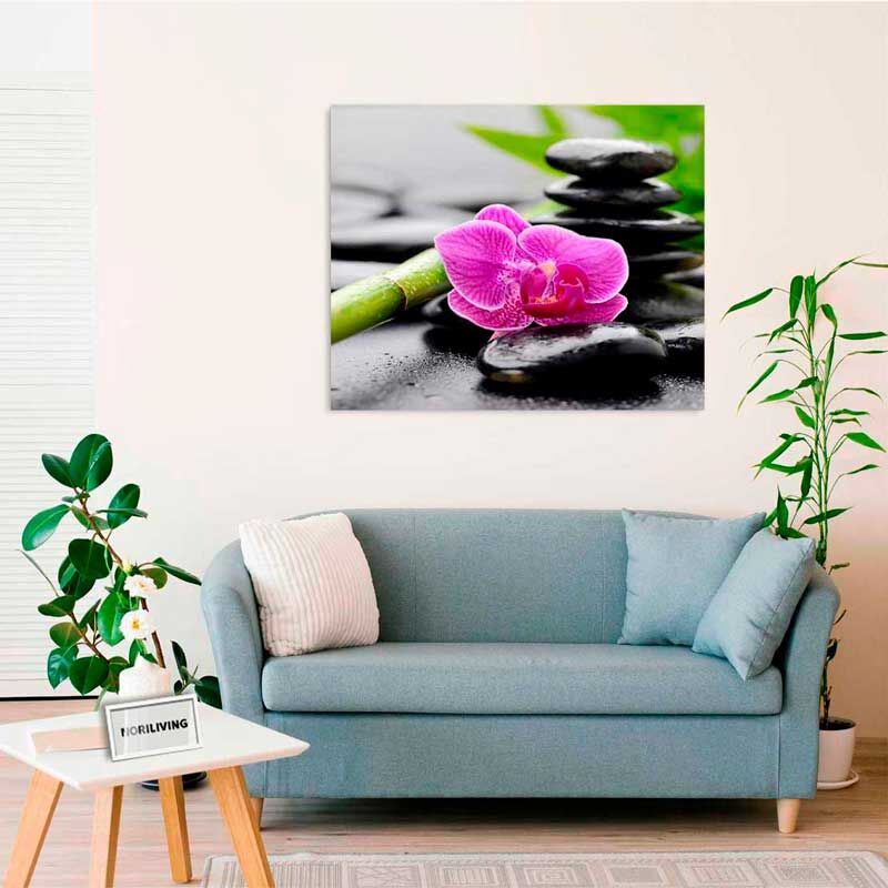 Ein Wohnzimmer mit blauem Sofa, Zierkissen und Wanddekoration featuring ein Zen-Motiv mit rosa Orchidee und Bambus vor einer Steinschichtung.