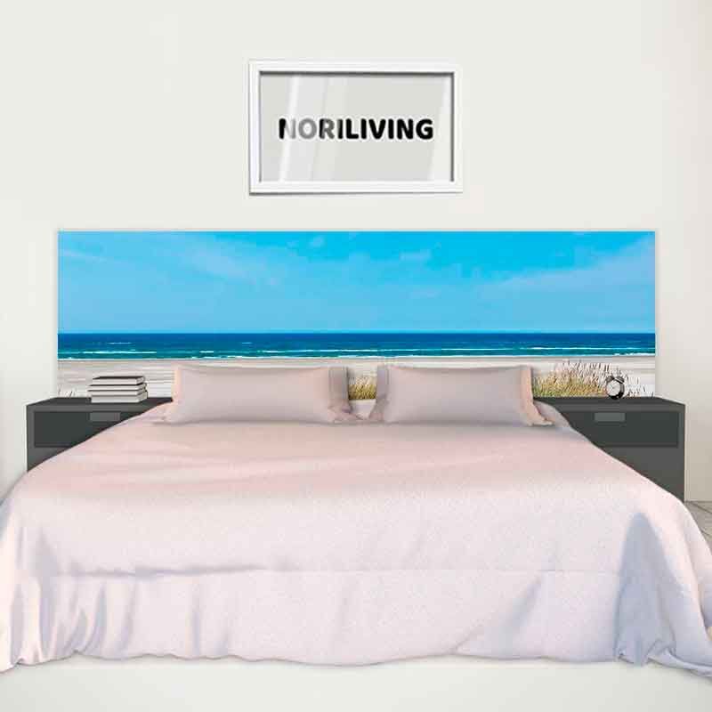Ein Bett mit einem Kopfteil mit Strandmotiven, flankiert von schwarzen Nachttischen. Darüber hängt ein gerahmtes Bild mit dem Schriftzug 'NORILIVING'.