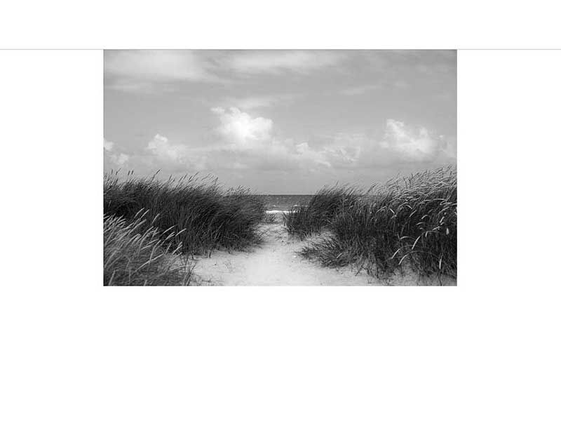 Ein Sandpfad führt durch Dünengras zum Meer unter einem teilweise bewölkten Himmel.