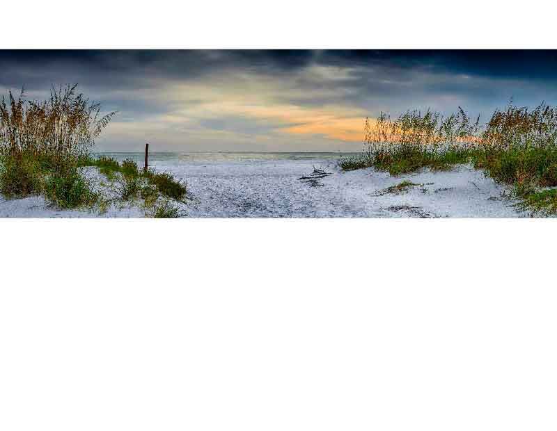 Ein Sandstrand mit Dünen und Blick auf das Meer bei Sonnenuntergang, der Himmel ist teils bewölkt.