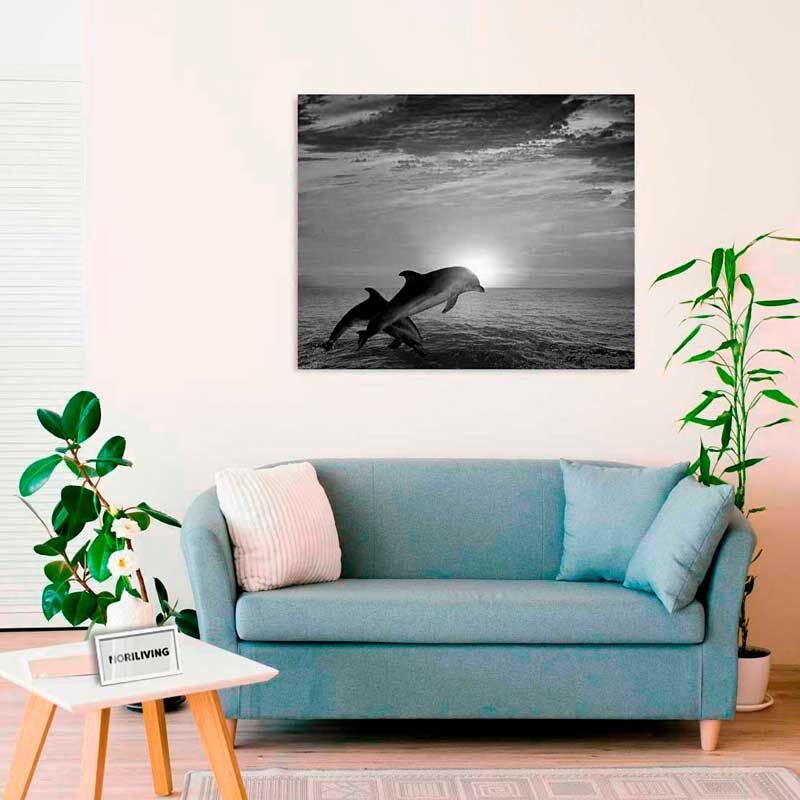 Wohnzimmer mit blauer Couch, Pflanzen und einem schwarz-weißen Bild von springenden Delfinen vor Sonnenuntergang an der Wand