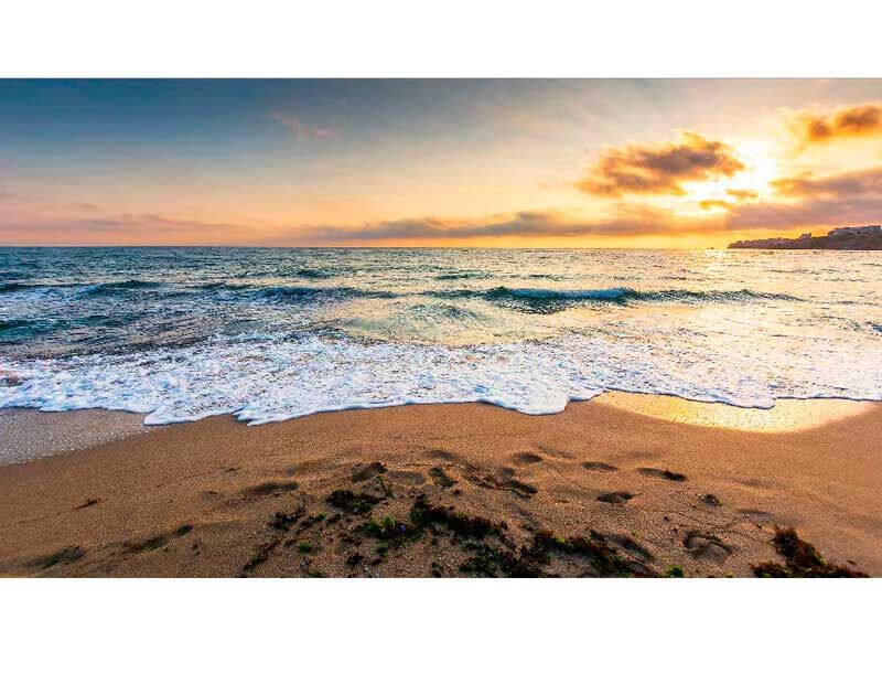 Malerischer Strand bei Sonnenuntergang mit sanften Wellen und Fußspuren im Sand