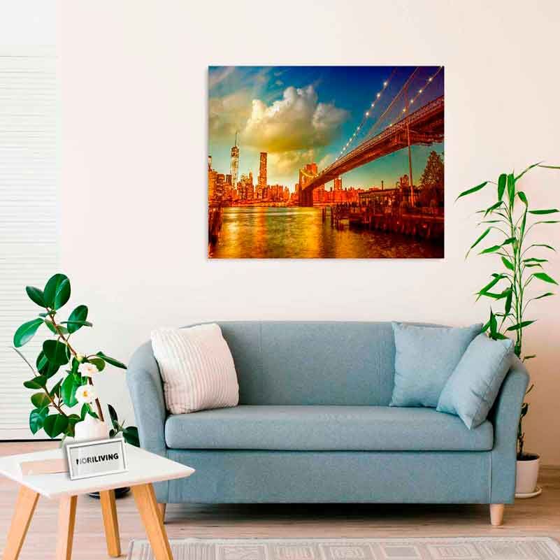 Wohnzimmer mit einer zweisitzigen blauen Couch, Pflanzen und einem großen Leinwandbild der Brooklyn Bridge bei Sonnenuntergang an der Wand