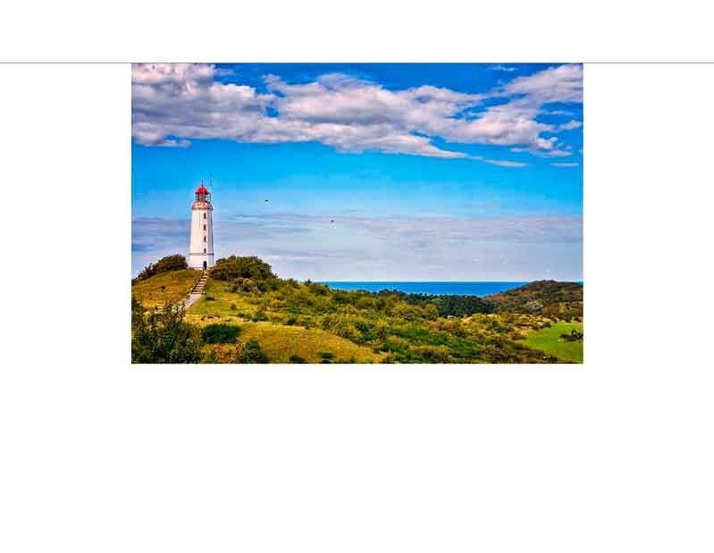 Ein weißer Leuchtturm mit roter Kuppel steht in einer grünen Landschaft unter einem blauen Himmel mit Wolken.