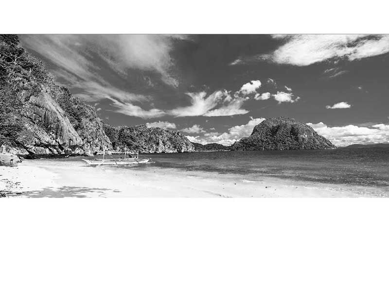 Ein Boot liegt an einem ruhigen Strand mit Felsen im Hintergrund unter einem wolkenbedeckten Himmel.
