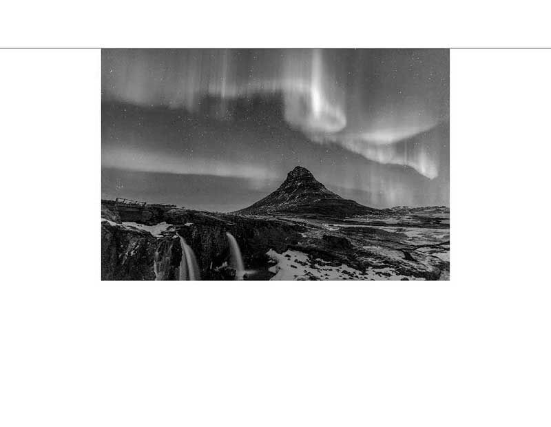 Schwarz-Weiß-Foto von Nordlichtern über einem Berg und Wasserfall im Winter