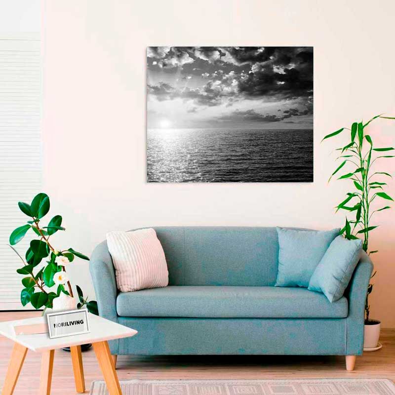 Ein helles Wohnzimmer mit einer blauen Couch, einem weißen Kissen und einem schwarz-weißem Bild von Meer und Wolken an der Wand
