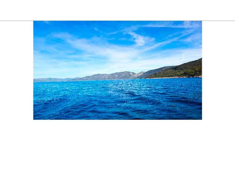 Blick auf das blaue Meer mit bewaldeten Hügeln unter einem klaren Himmel