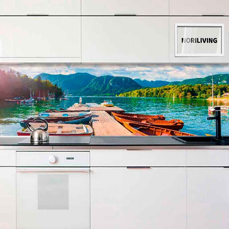 Weiße Küche mit einer Rückwand, die ein Dock mit Booten, einen See und Berge im Hintergrund zeigt.