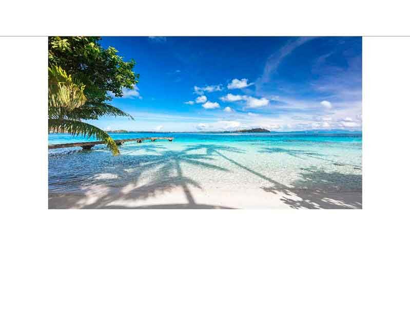 Ein tropischer Strand mit weißem Sand, klarem türkisblauem Wasser und Palmen im Vordergrund unter einem strahlend blauen Himmel.