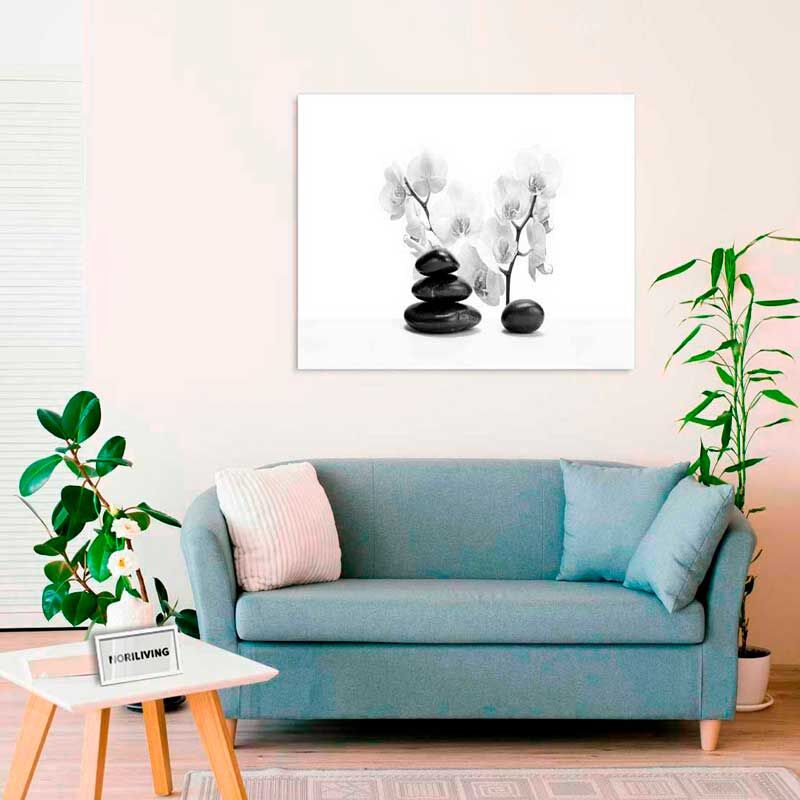 Gemütliches Wohnzimmer mit blauer Couch, weißem Tisch und Pflanzen. An der Wand hängt eine Leinwand mit Zen-Motiv, das Orchideen und Steine zeigt.