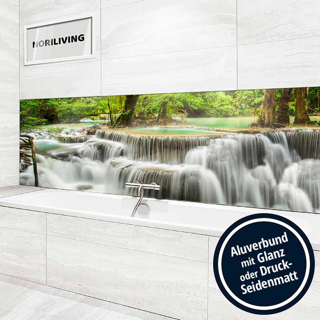 Moderne Badewanne mit hintergründigem Wasserfallbild auf einer Aluverbundplatte, umgeben von weißen Fliesen.