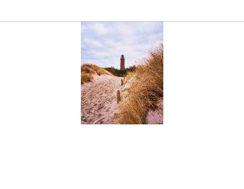 Ein Leuchtturm erhebt sich in einer Küstenlandschaft mit Dünen und Gras unter bewölktem Himmel