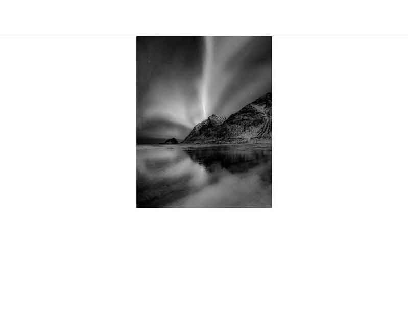 Schwarzweiß-Fotografie von Nordlichtern, die über einem Berg am Meer erscheinen
