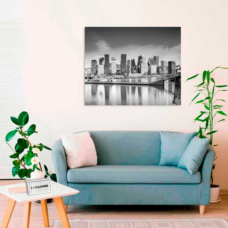 Ein stilvolles Wohnzimmer mit grauem Sofa, grünem Pflanzenschmuck und einem großen Schwarz-Weiß-Stadtbild an der Wand.