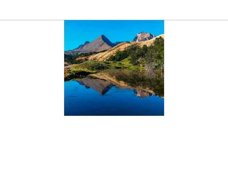 Ein malerischer See in den Alpen spiegelt die umliegenden Berge und den blauen Himmel wider.