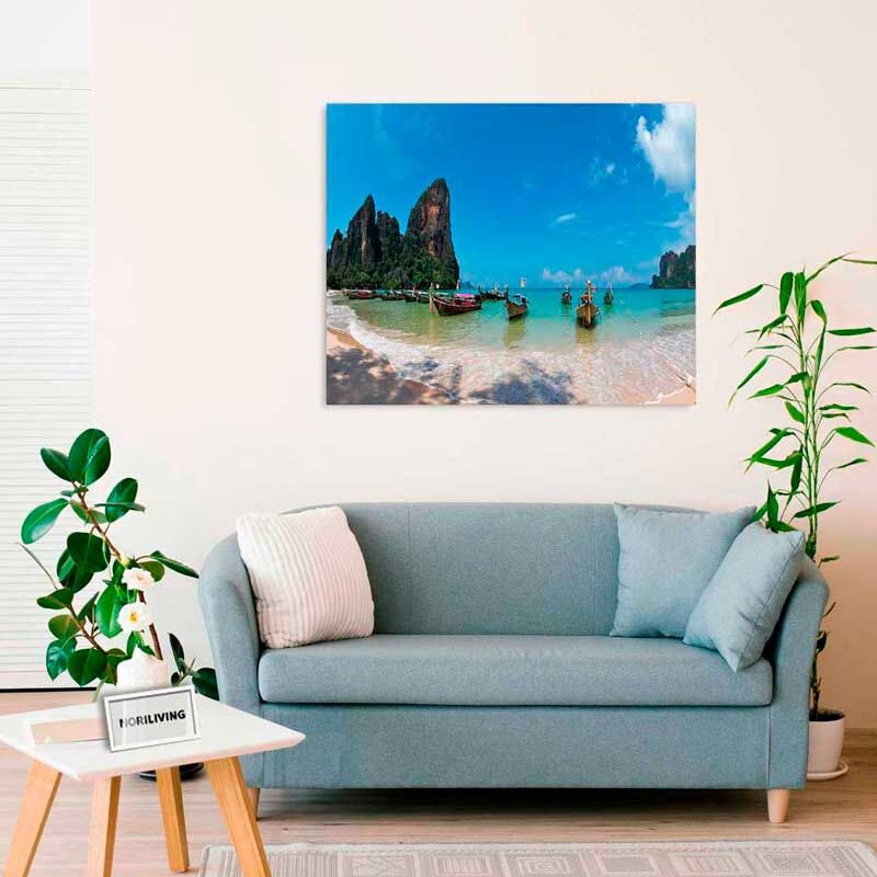 Ein Wohnzimmer mit einem blauen Sofa, Pflanzen und einem Wandbild eines tropischen Strands mit Booten und Felsen.